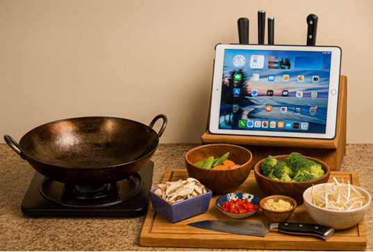 Wok cooking station with fresh vegetables and an iPad recipe display